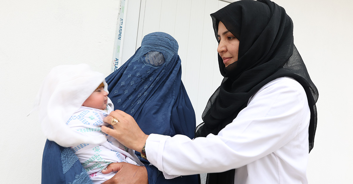 En barnmorska. till höger. undersöker en bebis som hålls av en kvinna i burka.