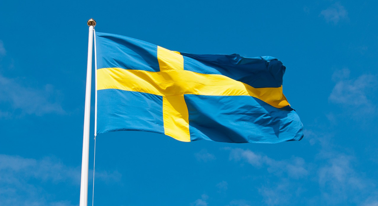 Foto på svenska flagga, blå med gult kors, mot en blå himmel