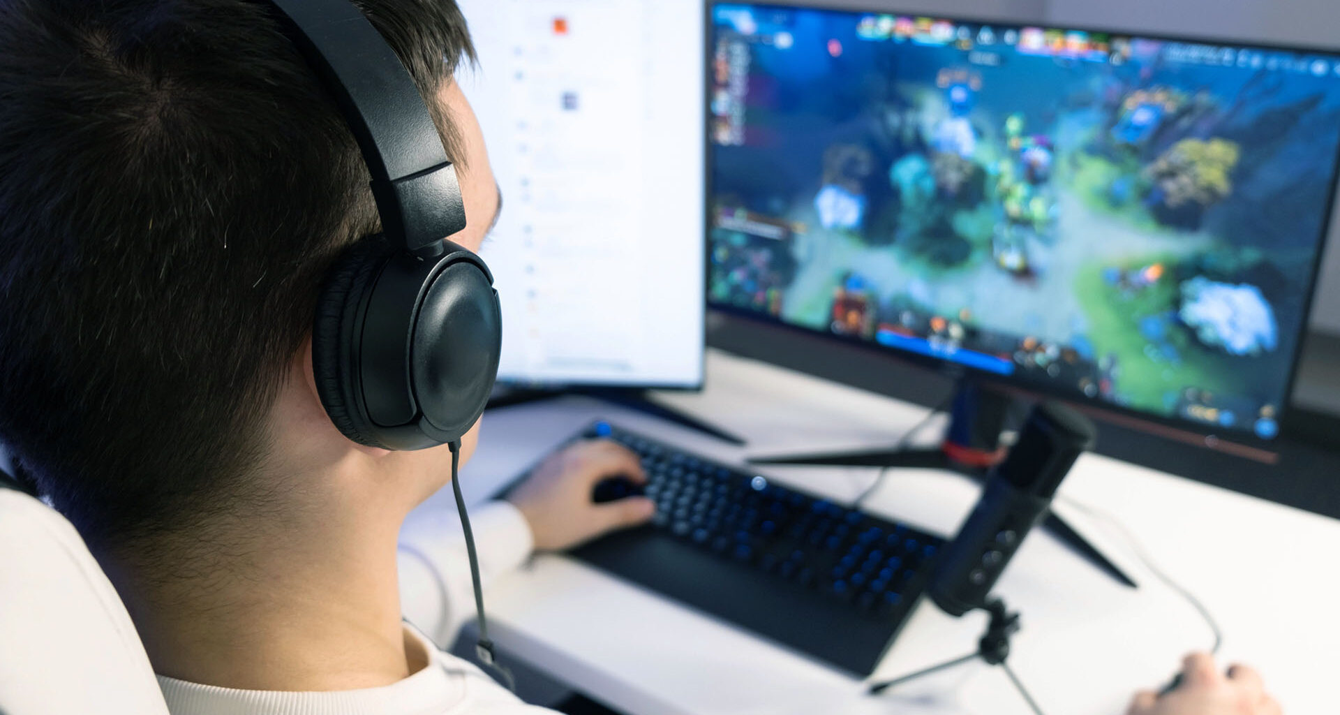 Tonårskille med hörlurar sitter framför datorskärm och spelar.