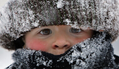 Ett barn tittar fram under en vintermössa med snö på.