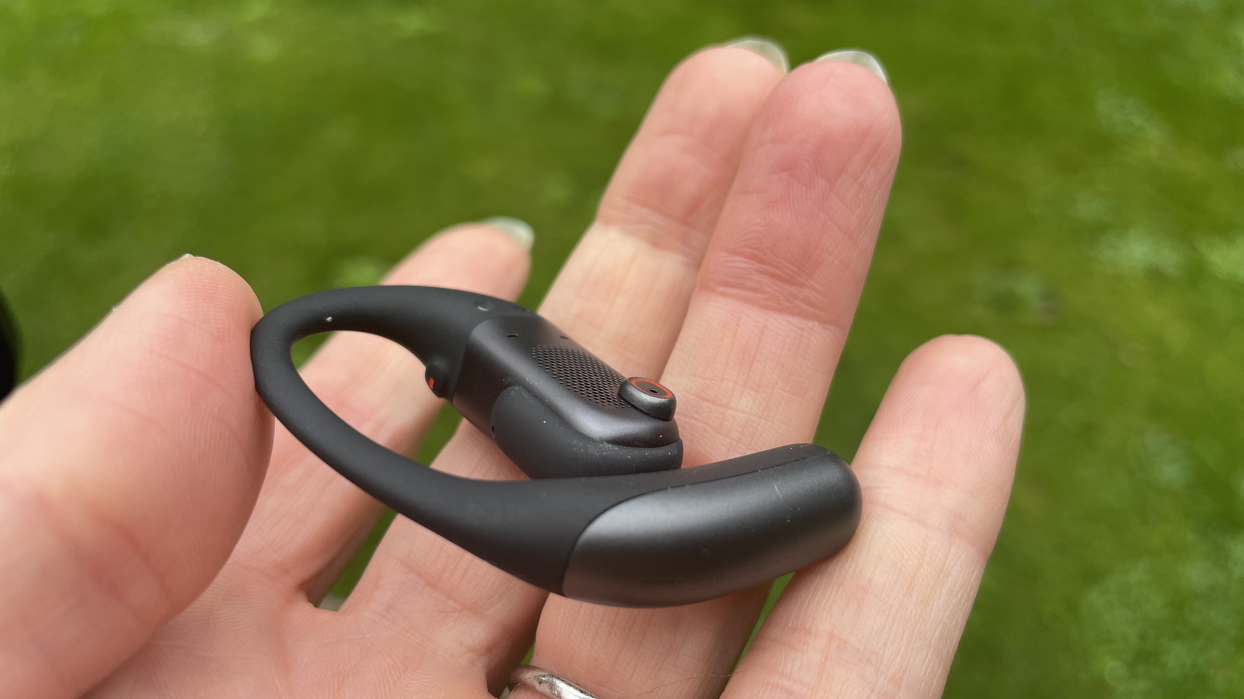 Shokz Openfit Pro hålls upp över en gräsmatta.