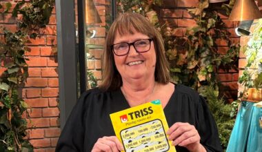 Person håller en Trisslott framför en dekorativ vägg med växter i bakgrunden.