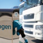 En vit lastbil i bakgrunden, en pump i förgrunden. På pumpen står det Hydrogen.