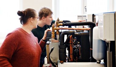 En man och en kvinna tittar nyfiket in i en värmecentral och läser av en mätare. 