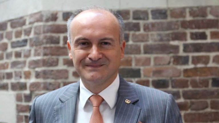 George Theocharidis ser in i kameran iförd kostym och slips.
