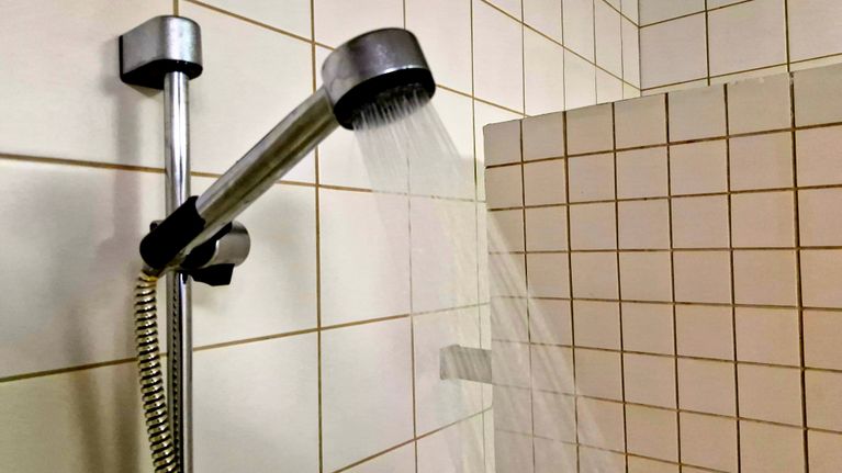 En duschslang med munstycke sprutar vatten i ett kaklat badrum.