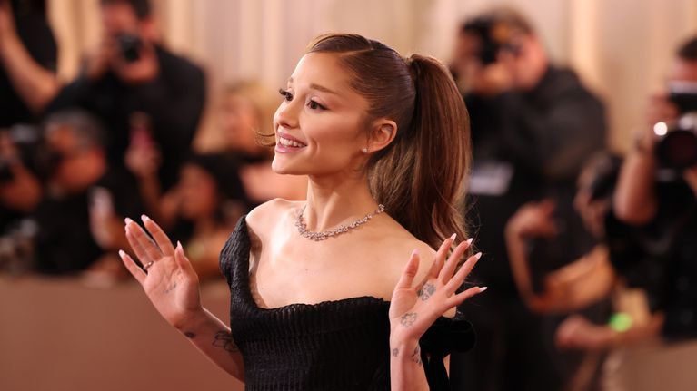 Ariana Grande står på röda mattan framför fotografer i bakgrunden.