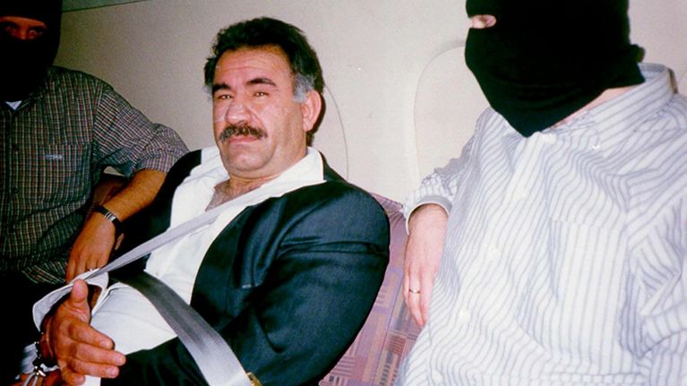 En gammal bild där Abdullah Öcalan sitte ri handfängsel mellan två män i rånarluvor.