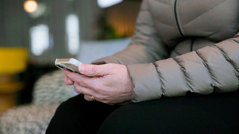 Närbild på kvinnas händer, hon håller i mobiltelefon.