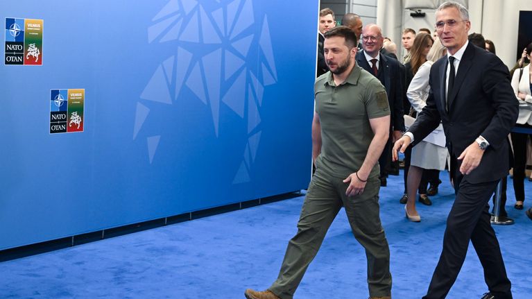Volodymyr Zelenskyj och Jens Stoltenberg går bredvid varandra på en blå matta.
