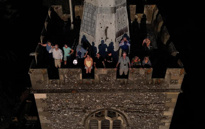 Fotografija z dronom, na kateri so ljudje s posebnimi zaščitnimi očali opazovali delni sončni mrk na vrhu zvonika cerkve sv. Marije v Rickmansworthu v Veliki Britaniji. FOTO: Suzanne Plunkett/Reuters
