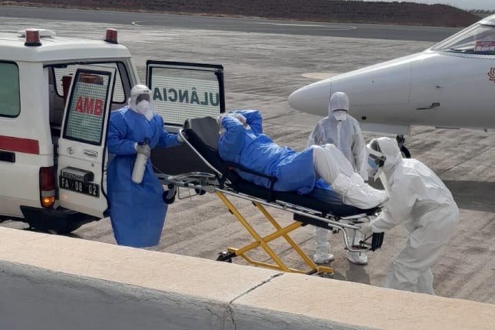 A person in a hazmat suit lies on a stretcher as other people in hazmat suits put the stretcher into the back of an ambulance.
