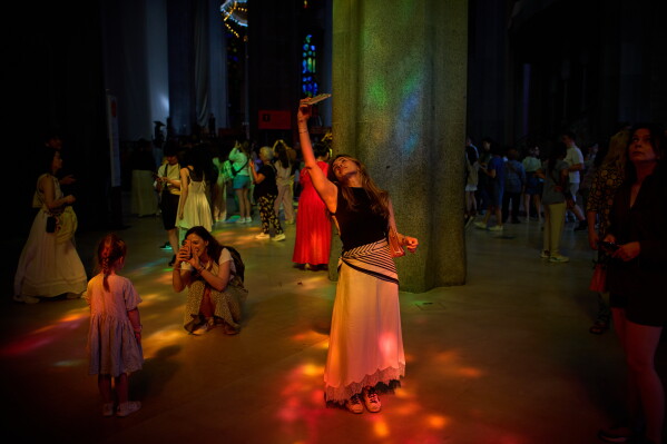 Visitors take photos inside Antoni Gaudí's Basilica of the Sagrada Familia as colored light from its stained-glass windows illuminates the interior in Barcelona, Spain, Tuesday, May 26, 2026, ahead of Pope Leo XIV's visit to the city in June. (AP Photo/Emilio Morenatti)