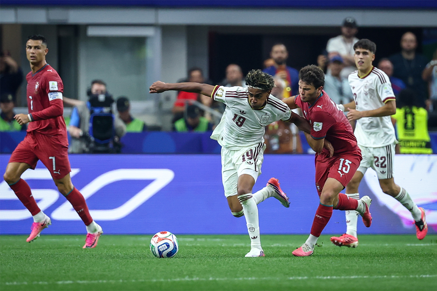 Spain's Lamine Yamal shields the ball from a challenging Portugal defender, arm extended for balance as he drives forward.
