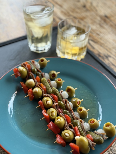 skewers with olives, vegetables and pickles next to two glasses of vermouth