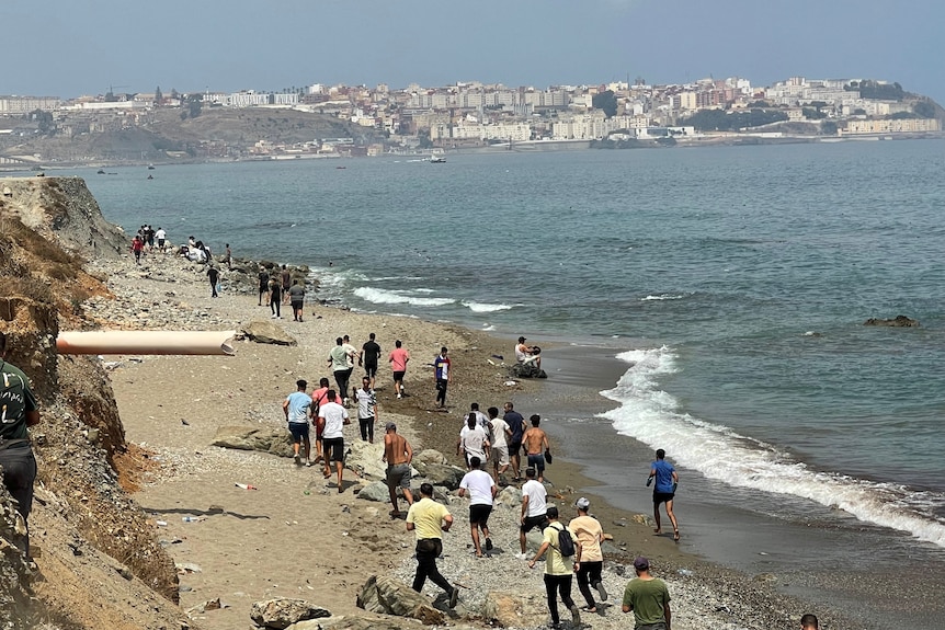 A group of people walk along a beach, clothes soaked