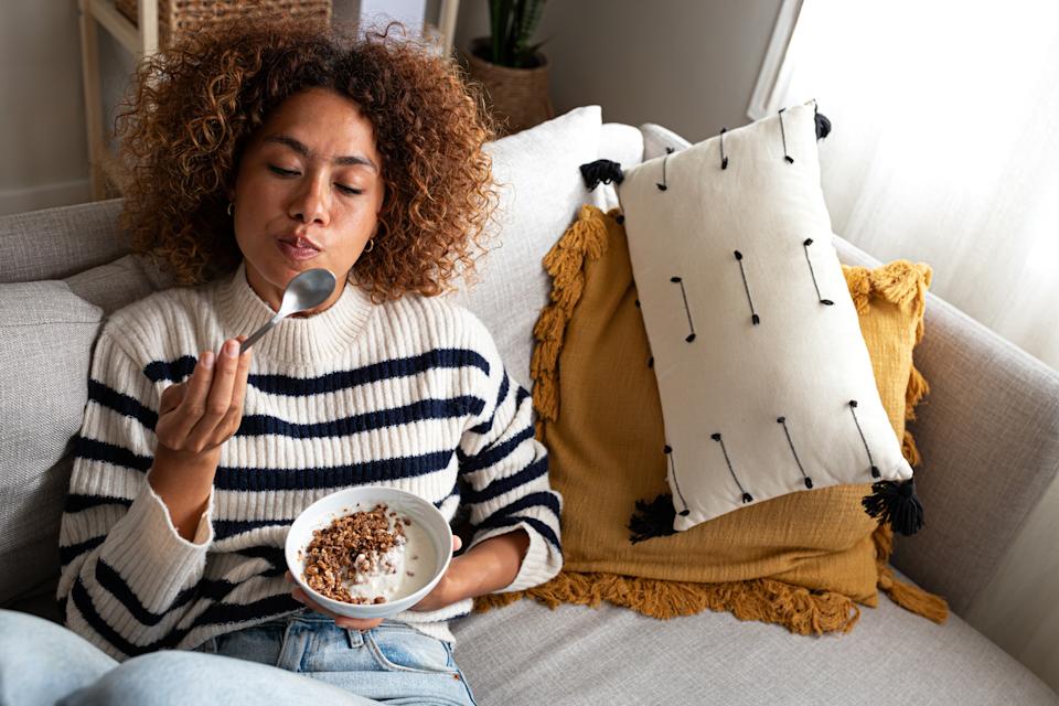 Person relaxing on a couch, wearing a striped sweater, eating from a bowl. Cozy pillows are in the background