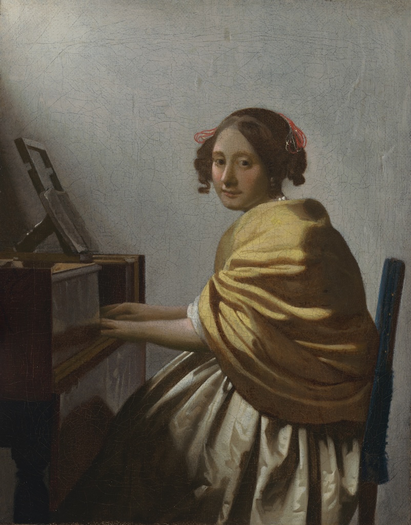 A lovely Vermeer painting of a young woman in a yellow shawl seated at a virginal.