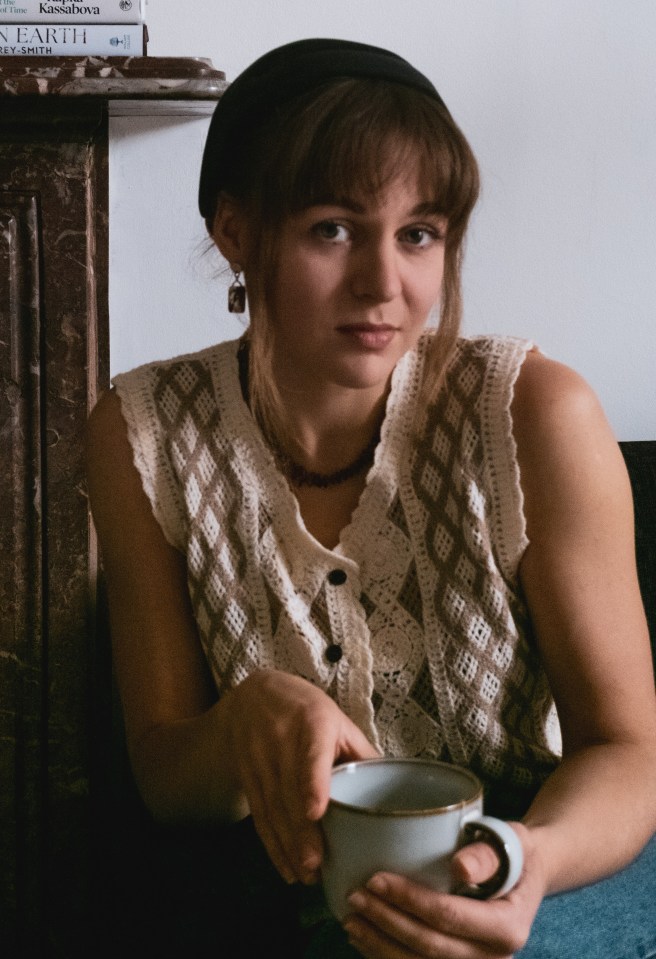 Woman holding a mug, sitting in front of a stack of books.