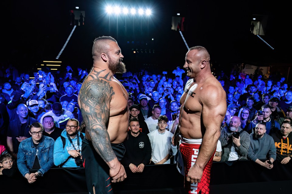 Two shirtless strongmen facing each other in front of a crowd.