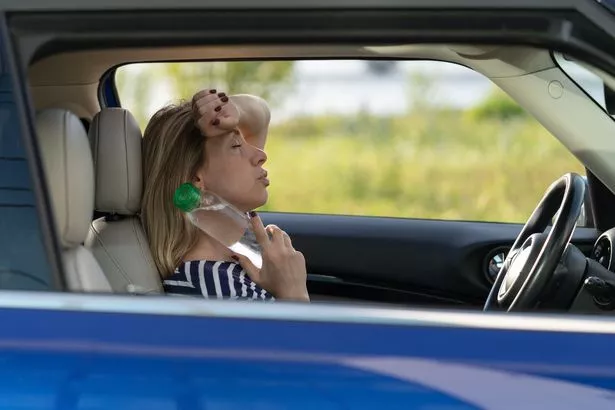 This is a photo of a woman sat in a car struggling with heat exhaustion