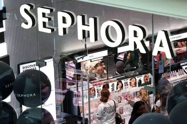 Close up on Sephora store sign. Below people seen browsing makeup products