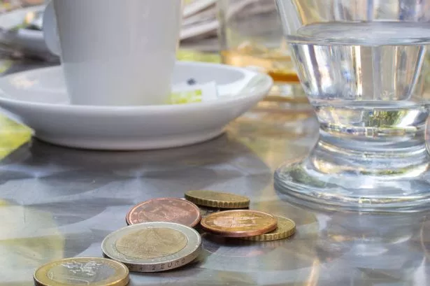 Image of coins left on table as a tip with mug and glass behind 