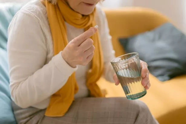 Close up view of unrecognizable mature woman taking a pill. She has a pill in one hand and a glass of water in the other.
