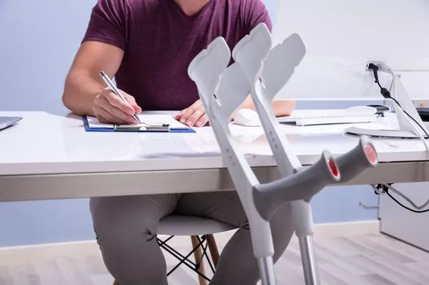 Close-up Of Crutches Leaning On Table In Front Of Handicapped Man Filling Form