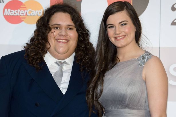 Jonathan Antoine and Charlotte Jaconelli wearing a suit and silver dress on a Mastercard red carpet