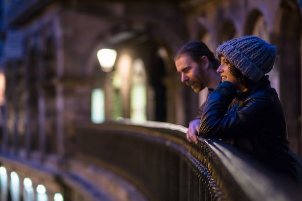 A man and woman are leaning on the railing of Victoria Terrace, Edinburgh at night.