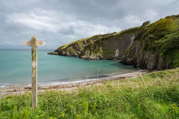 A sign for the coast path above the beach at Aberfforest, with a bright blue sea in the background