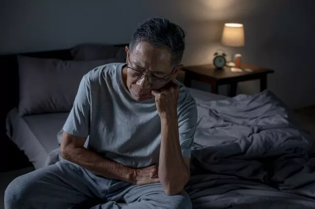 Depressed senior Asian man sitting in bed cannot sleep from insomnia