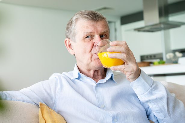 Cheerful senior man drinking orange juice at home