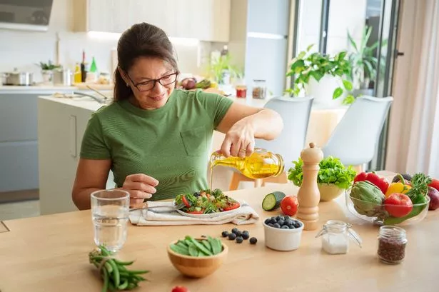 Woman sitting at the table dressing  fresh organic vegetables salad plate with olive oil