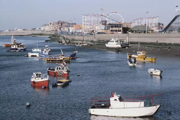 Boats are moored in view of the funfair and rollercoaster rides at the seaside town of Rhyl, on the north east coast of Wales, June 1983