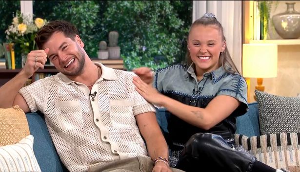 Chris Hughes, in a beige top and brown trousers, sat next to JoJo Siwa, in a blue and black top, and black trousers, on the This Morning sofa.
