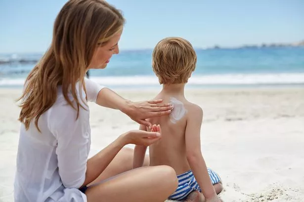 Mother applying sun cream to her son on the beach.