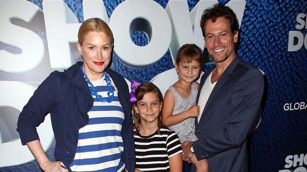 A husband and wife with two girls, standing on a red carpet and smiling