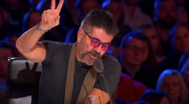 Simon Cowell in a black top and brown scarf on the Britain's Got Talent judging panel.