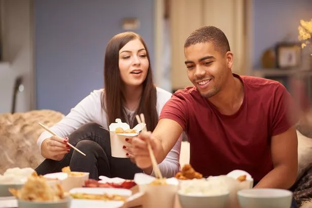 A young couple sit on the sofa and share a meal