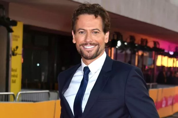 A picture of man in a navy suit and tie standing on a red carpet