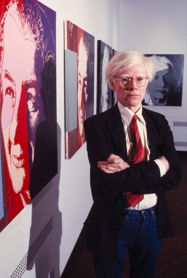 Andy Warhol standing in front of his artwork.