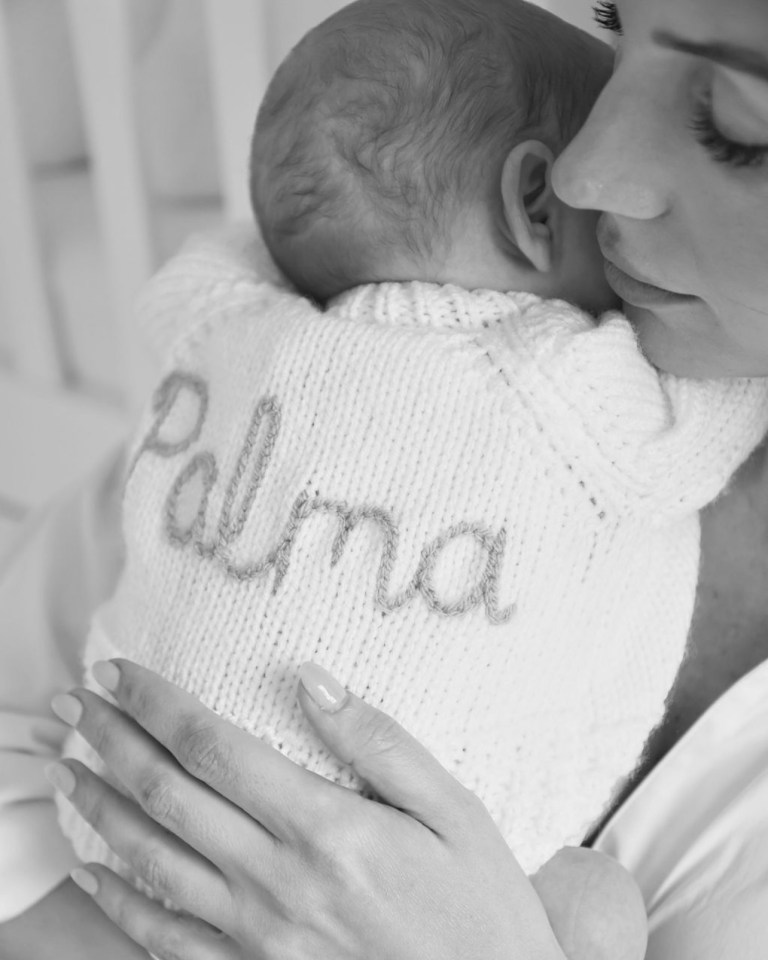 Black and white photo of a mother holding her baby, who is wearing a knitted sweater that says "Palma."