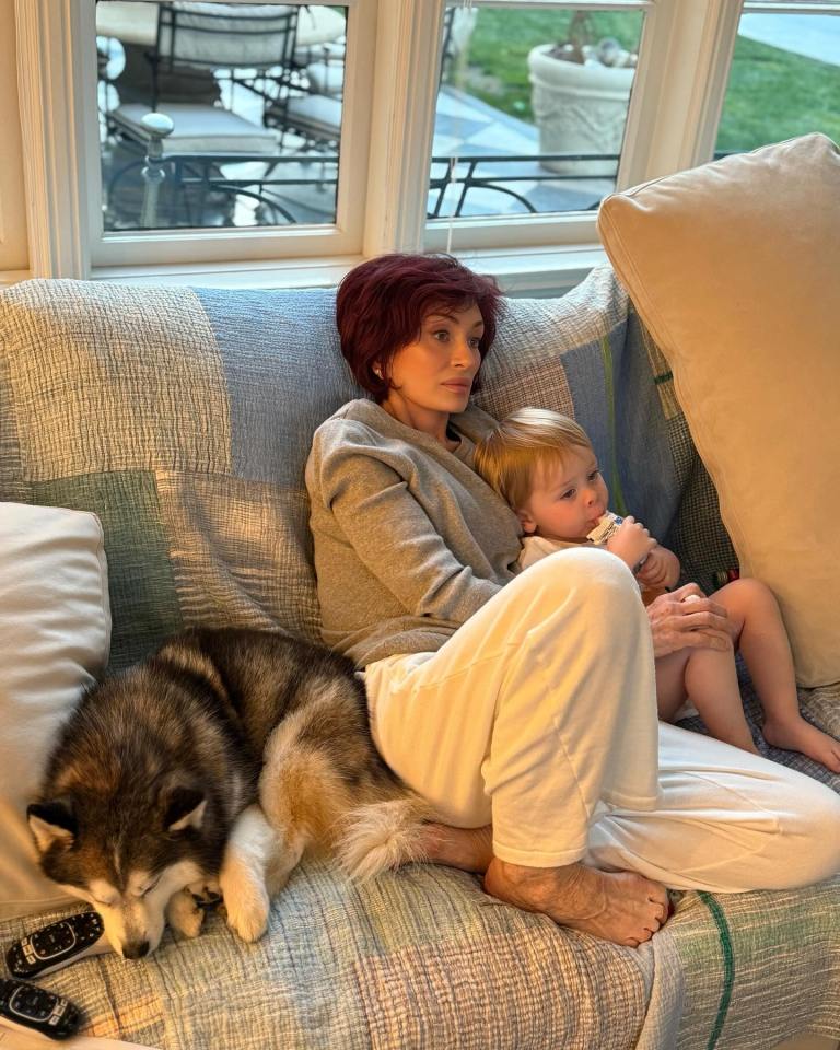 Sharon Osbourne cuddling a toddler and a dog on a couch.