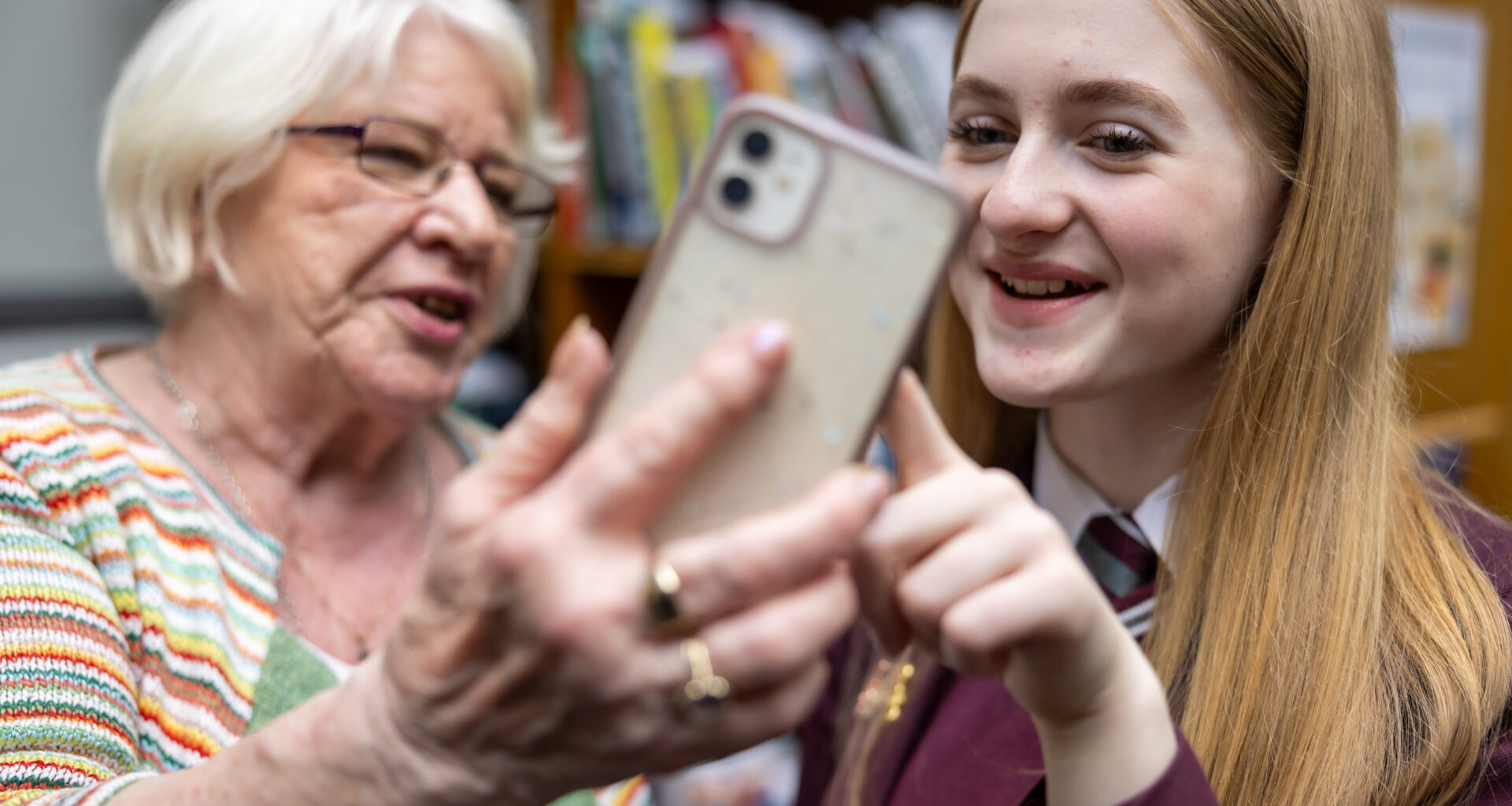 An older woman and teenage girl school pupil both smiling as they look at a mobile phone