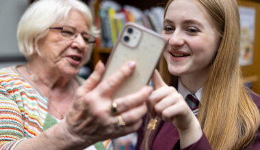 An older woman and teenage girl school pupil both smiling as they look at a mobile phone