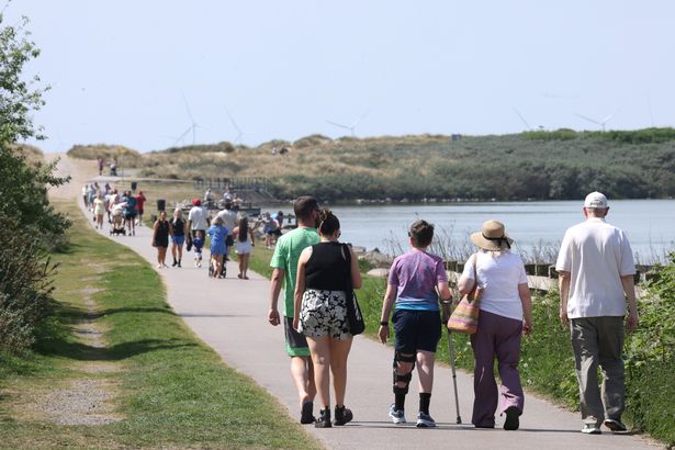 People make their way to make the most of the hot weather on Crosby beach this afternoon