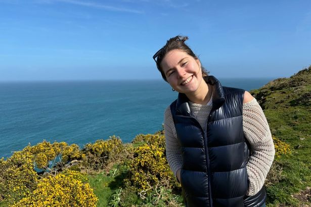A young woman smiling on a walk next to the bright blue sea
