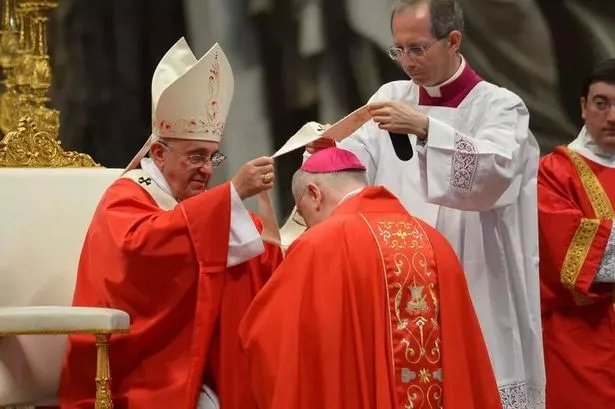 An image of the Pope bestowing the Pallium on to an Archbishop, both wearing red robes.